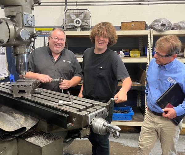 Logan and his Trainer Rob posing for a photo in front of a machine they use in the detail room.